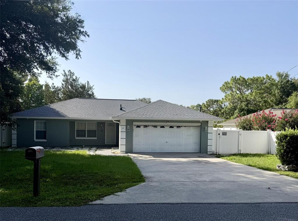 A single-story house with a gray exterior, white garage door, and a white vinyl fence — 11 PECAN PASS WAY, OCALA, FL