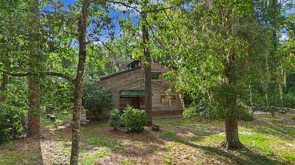 A two-story wooden house sits in a wooded yard with mature trees and shrubs — 2906 SE 36TH LANE, GAINESVILLE, FL