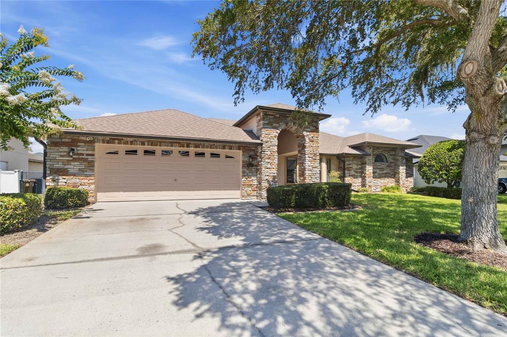 A single-story house with a stone facade, a two-car garage, and a large front tree — 122 LENA ANN DRIVE, ST CLOUD, FL