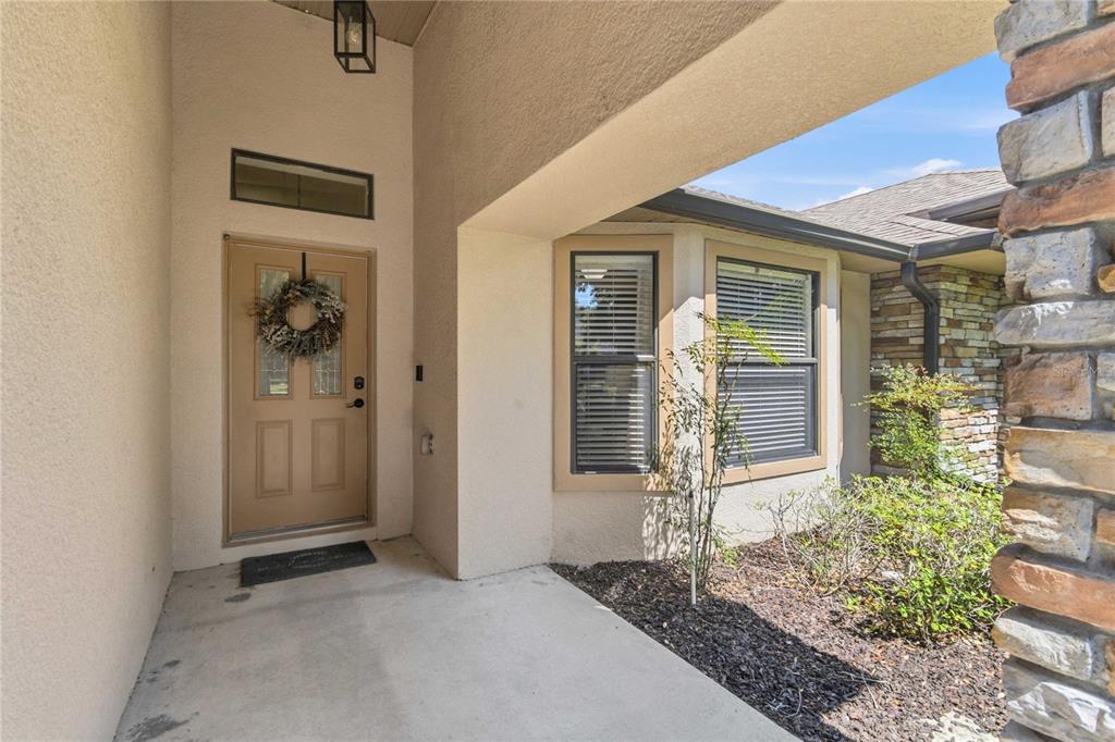 A covered entryway features a tan front door, a bay window, and stone exterior accents — 122 LENA ANN DRIVE, ST CLOUD, FL