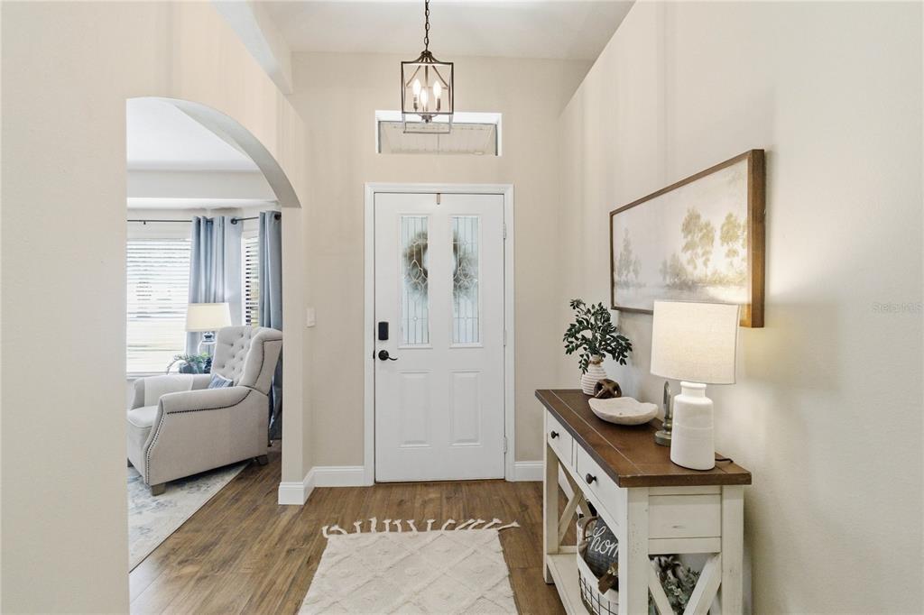 A bright entryway features wood-look flooring, a white front door, and a console table — 122 LENA ANN DRIVE, ST CLOUD, FL