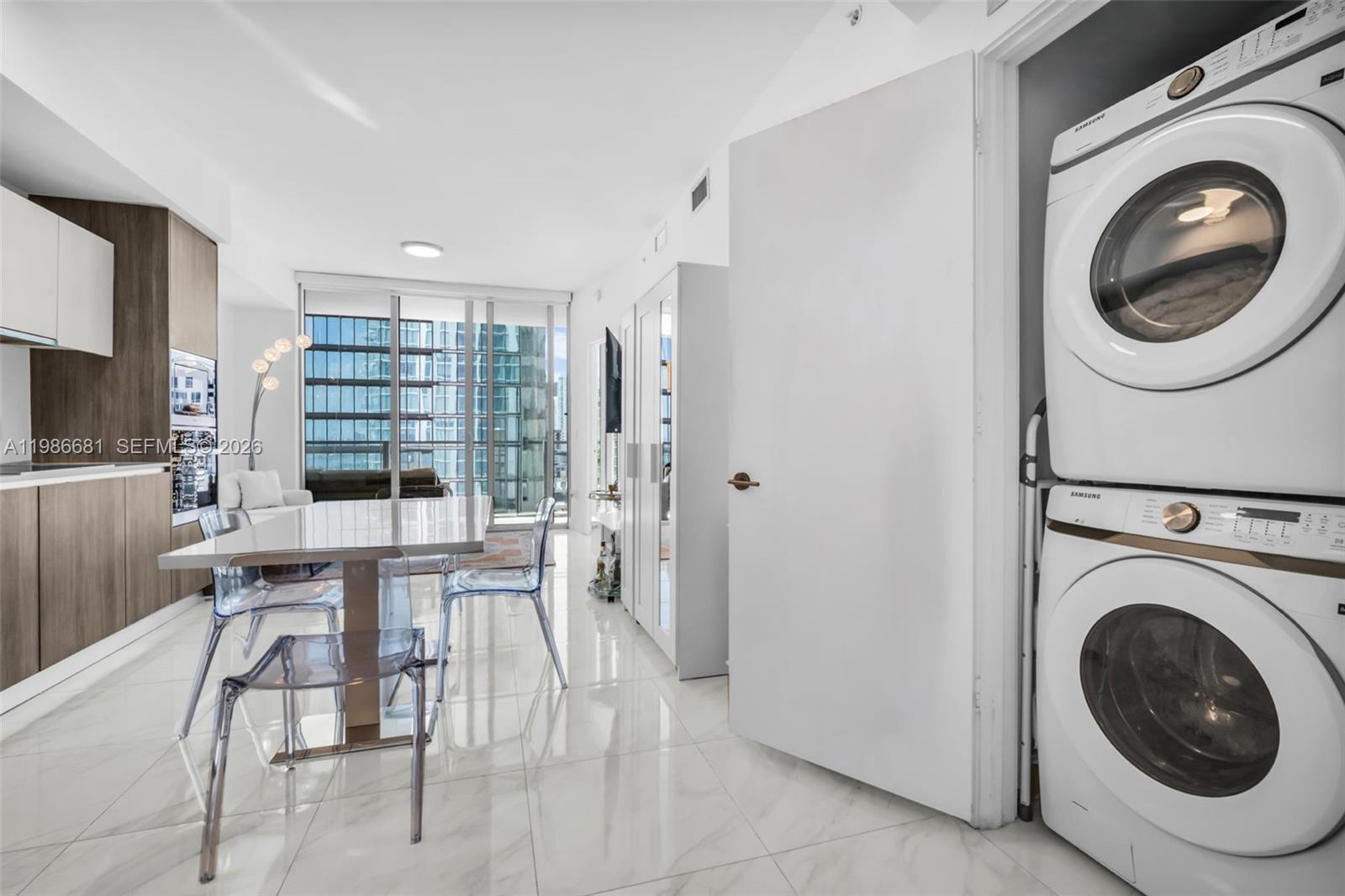 A modern kitchen and dining area features white tile floors, a stacked washer-dryer, and windows — 2900 NE 7th Ave # 1408, Miami FL 33137, MIAMI, FL