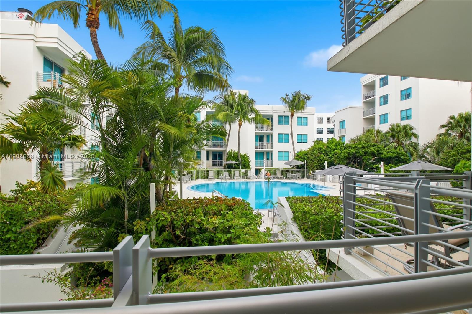 A view from a balcony overlooking a swimming pool surrounded by palm trees and buildings — 110 Washington Ave # 2420, Miami Beach FL 33139, MIAMI BEACH, FL