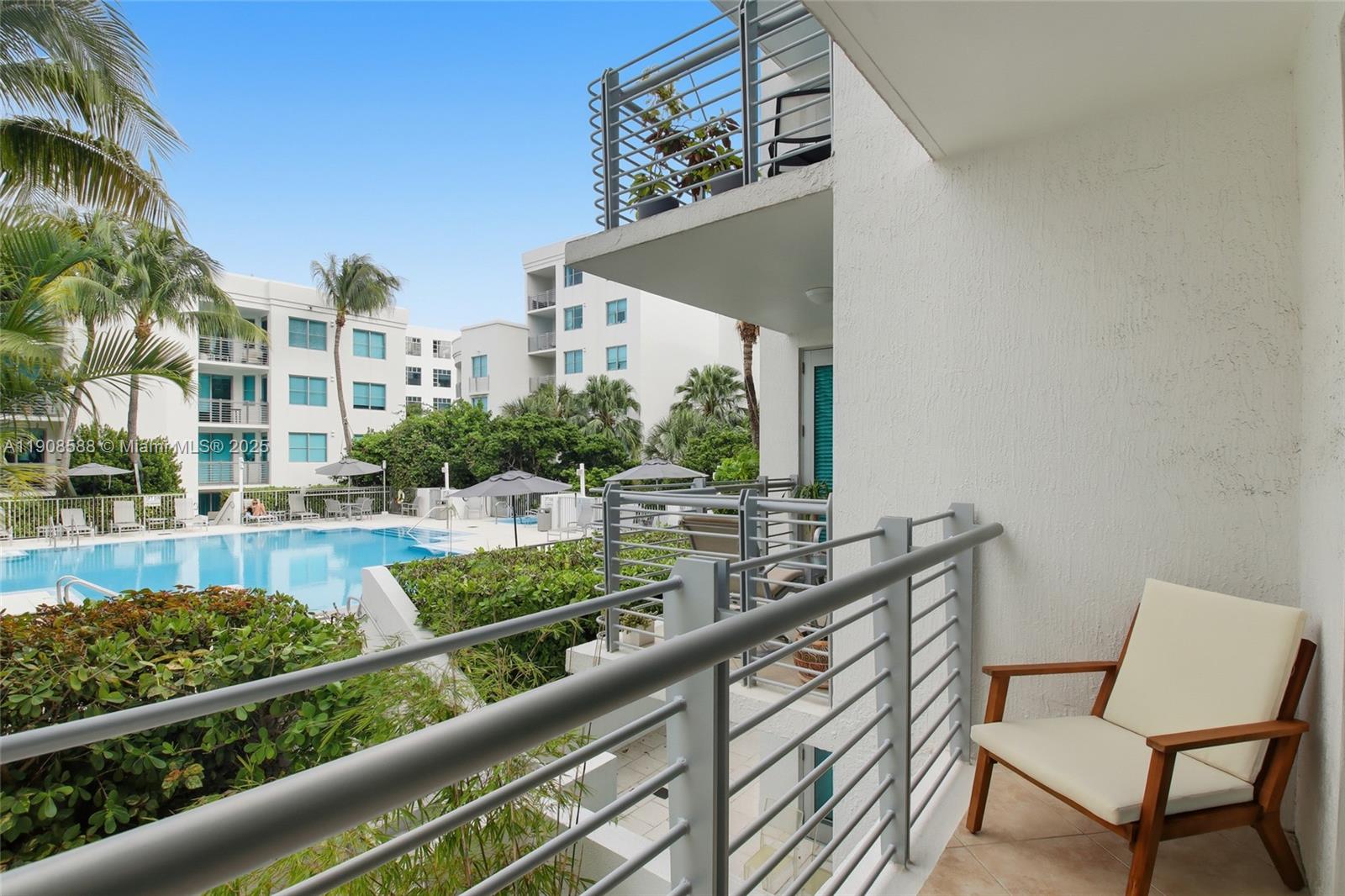 A balcony with a wooden chair overlooks a swimming pool and surrounding apartment buildings — 110 Washington Ave # 2420, Miami Beach FL 33139, MIAMI BEACH, FL