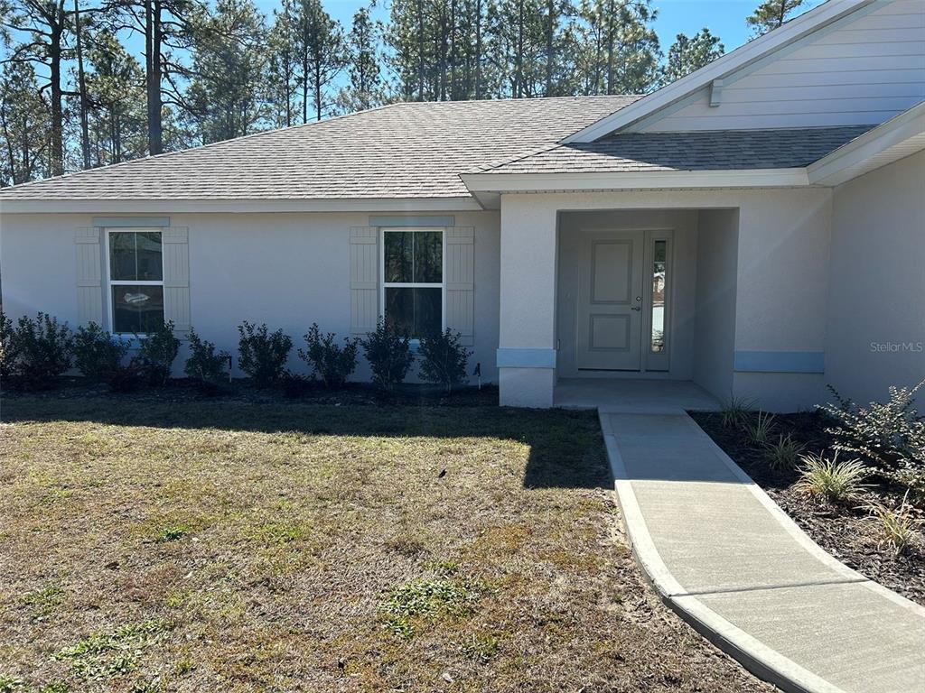 The exterior of a light-colored house features a front walkway, two windows, and a door — 1586 W GAINSBORO LANE, CITRUS SPRINGS, FL