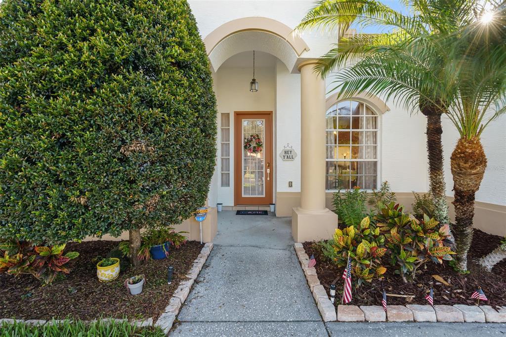 The front entrance of a house features a brown door, an arched porch, and landscaping — 12213 ROSELAND DRIVE, NEW PORT RICHEY, FL
