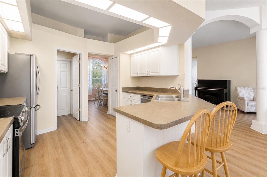 A kitchen with white cabinets, laminate countertops, and a breakfast bar overlooking a living area — 12213 ROSELAND DRIVE, NEW PORT RICHEY, FL
