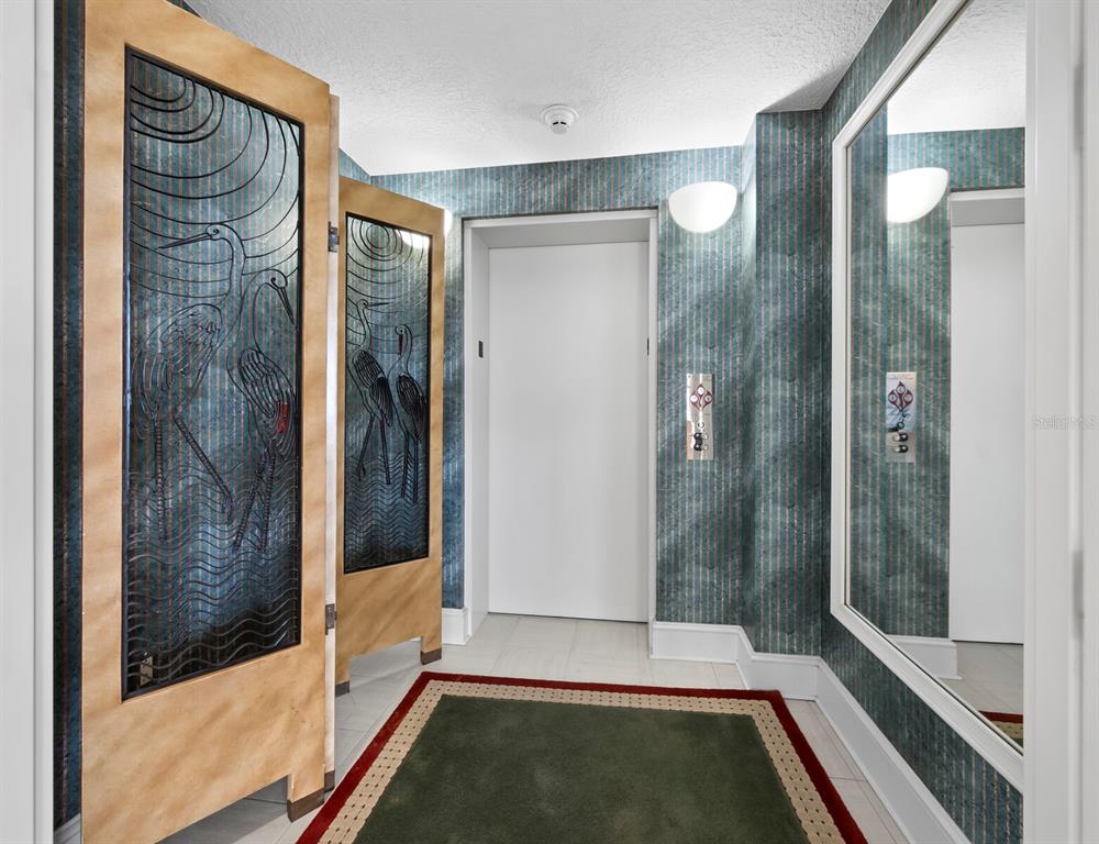 An elevator lobby features patterned wallpaper, decorative heron-etched glass doors, and a large wall mirror — 3040 GRAND BAY BOULEVARD UNIT 232, LONGBOAT KEY, FL
