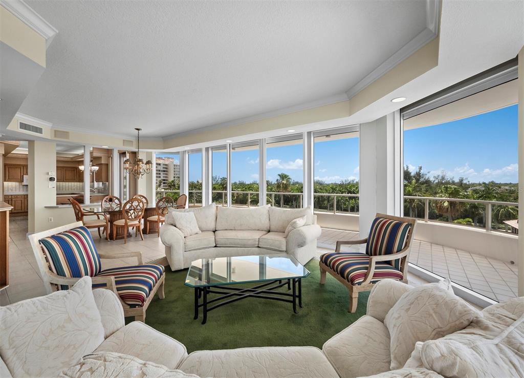 A living room with a curved sofa, striped armchairs, and floor-to-ceiling windows overlooking trees — 3040 GRAND BAY BOULEVARD UNIT 232, LONGBOAT KEY, FL