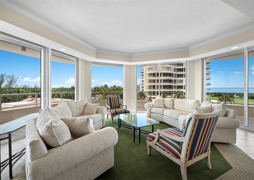 A living room with white sofas, striped chairs, a glass coffee table, and panoramic windows — 3040 GRAND BAY BOULEVARD UNIT 232, LONGBOAT KEY, FL