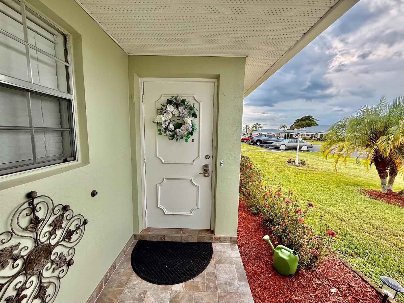 A light green exterior wall features a white front door with a floral wreath — 916 Savannas Point Drive, Fort Pierce FL 34982, FORT PIERCE, FL