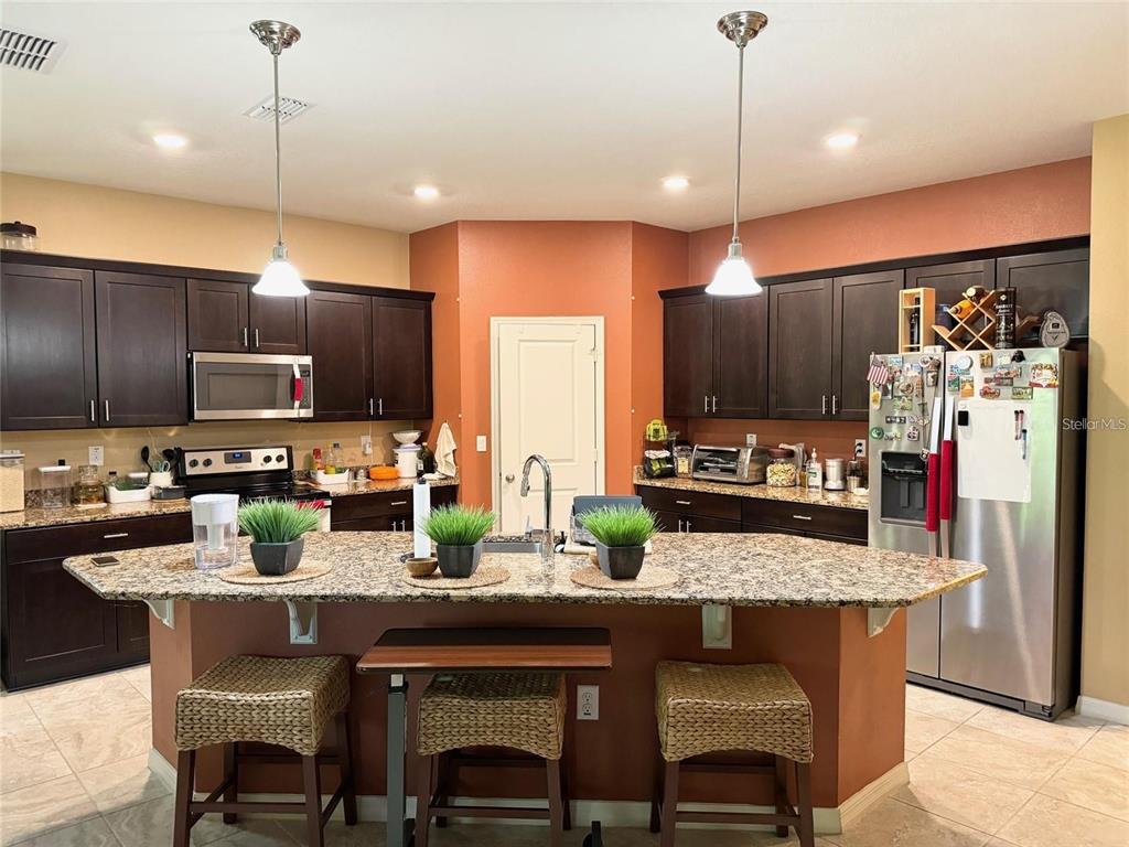 A kitchen with dark wood cabinets, granite countertops, a central island, and stainless steel appliances — 11460 WAKEWORTH STREET, ORLANDO, FL