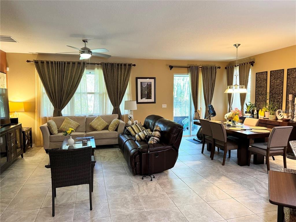 An open-concept living and dining area features tile flooring, neutral walls, and large windows — 11460 WAKEWORTH STREET, ORLANDO, FL
