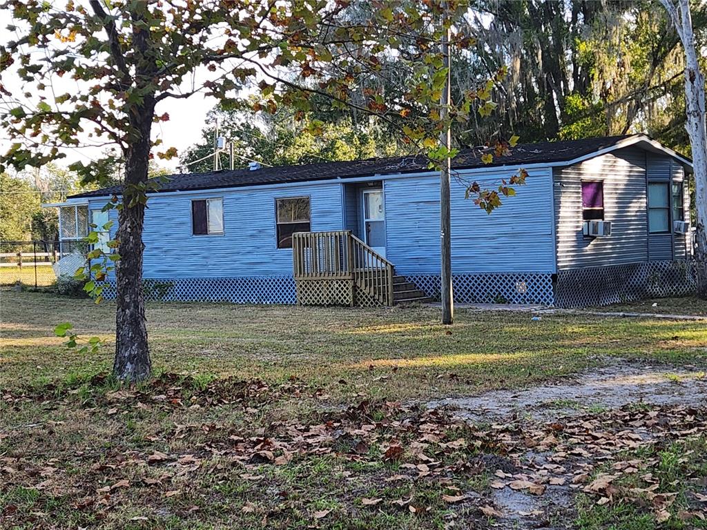A blue single-wide mobile home with a wooden front porch sits on a grassy lot — 2608 20 MILE LEVEL ROAD, LAND O LAKES, FL