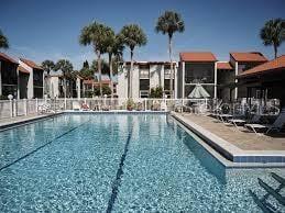 A swimming pool sits in front of a multi-story apartment complex with palm trees — 3215 BENEVA ROAD UNIT 204, SARASOTA, FL