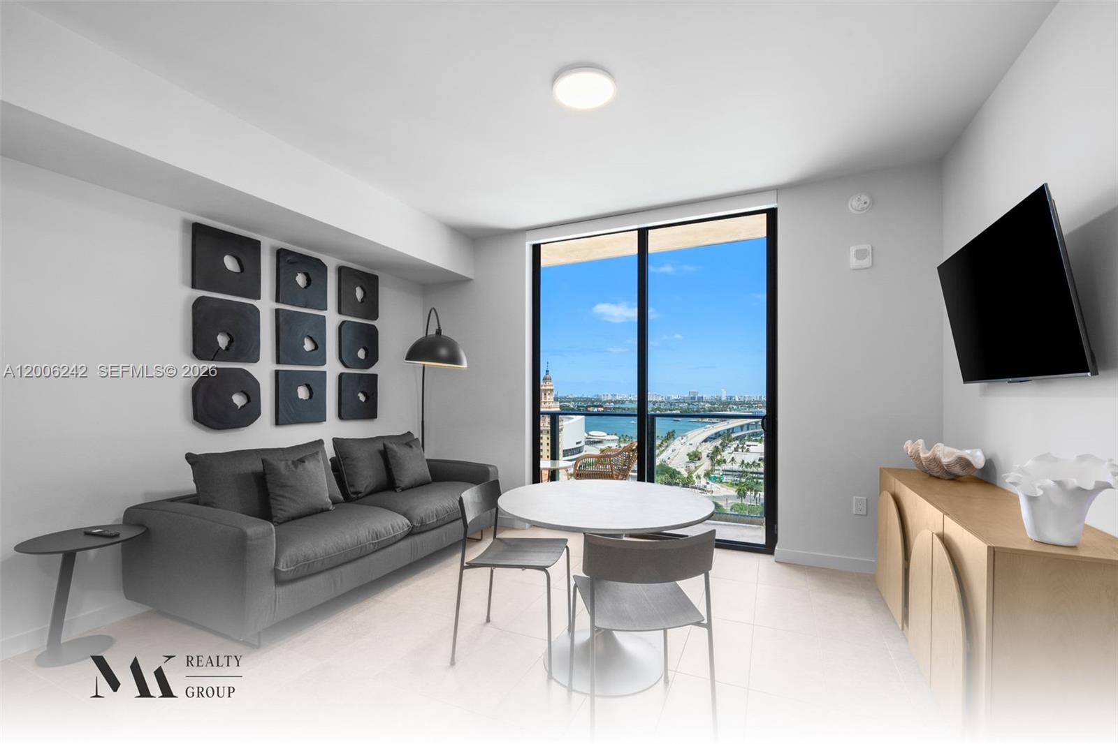 A modern living room features a grey sofa, dining table, and a balcony with water views — 121 NE 5 # 2700, Miami FL 33132, MIAMI, FL