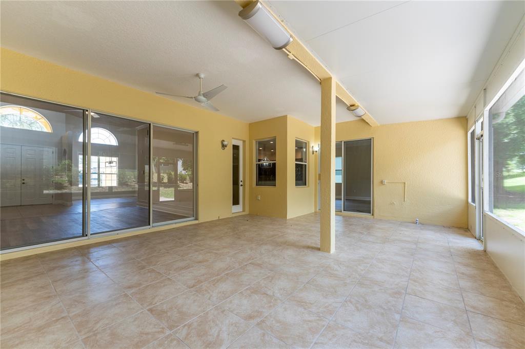 A covered patio with light-colored tile flooring, yellow walls, and large sliding glass doors — 3542 WIND RIVER RUN, CLERMONT, FL