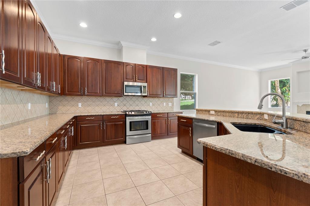 A kitchen features dark wood cabinets, granite countertops, stainless steel appliances, and tile flooring — 3542 WIND RIVER RUN, CLERMONT, FL
