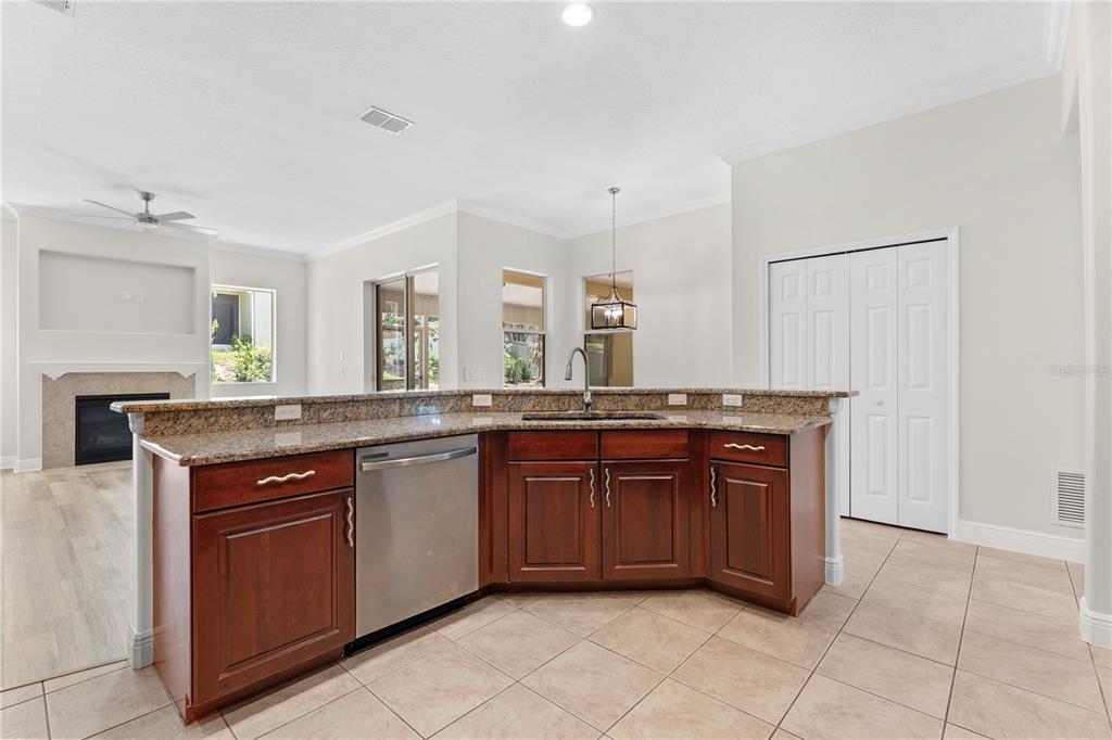 A kitchen island with a stainless steel dishwasher and granite countertops faces a living area — 3542 WIND RIVER RUN, CLERMONT, FL