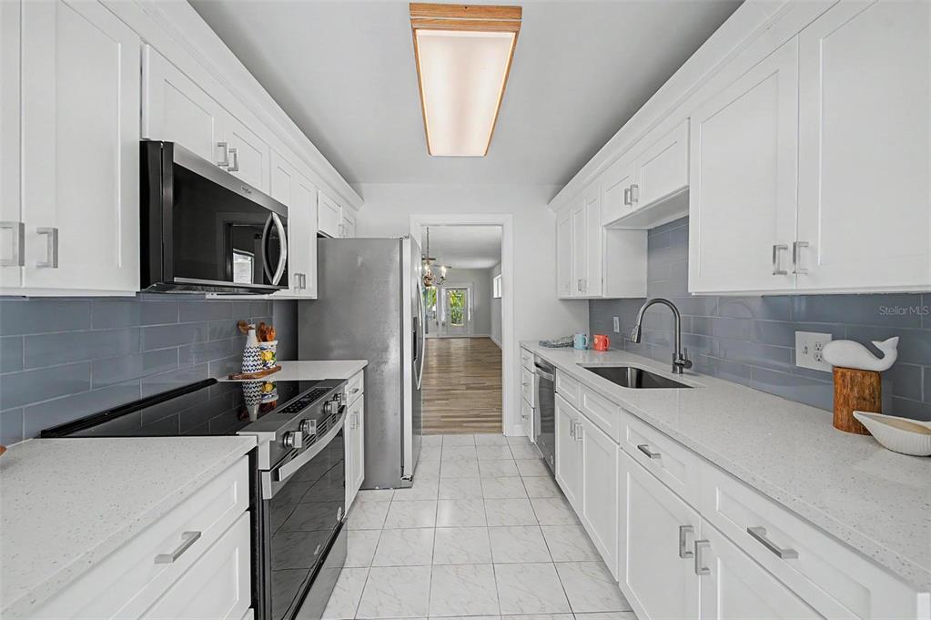 A galley kitchen features white cabinets, quartz countertops, a gray subway tile backsplash, and stainless appliances — 144 BOCA CIEGA POINT BOULEVARD N, ST PETERSBURG, FL