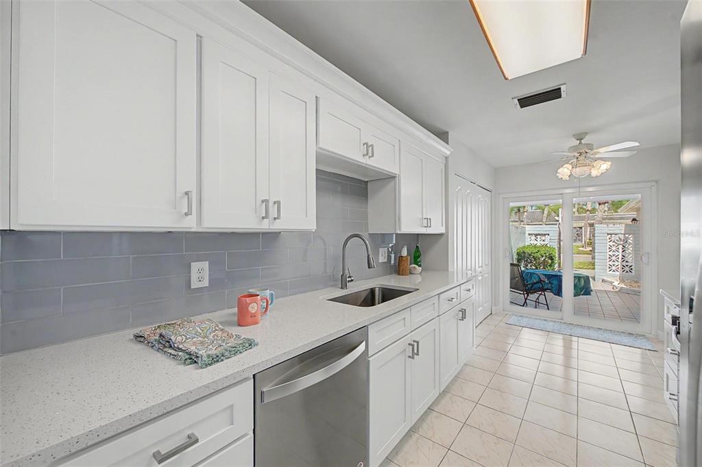 A galley kitchen with white cabinets, quartz countertops, and a dining area overlooking a patio — 144 BOCA CIEGA POINT BOULEVARD N, ST PETERSBURG, FL