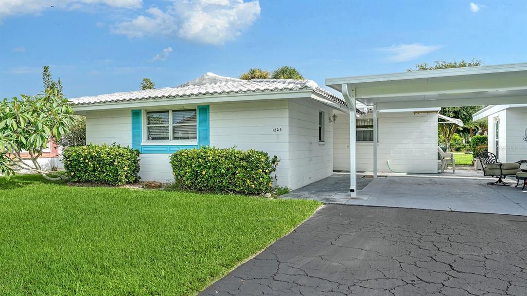 A white single-story house with a carport, a paved driveway, and green landscaping — 1523 LAKESIDE DRIVE UNIT 15, VENICE, FL