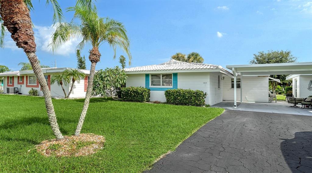 A white single-story house with a carport, palm trees, and a green lawn — 1523 LAKESIDE DRIVE UNIT 15, VENICE, FL