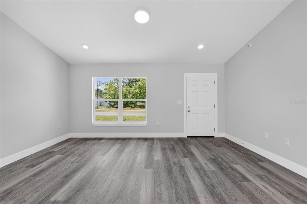 An empty room with gray walls, wood-look flooring, a window, and a white door — 13155 SW 70TH COURT, OCALA, FL