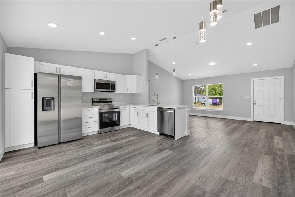 A modern kitchen with white cabinets, stainless steel appliances, and gray wood-look flooring — 13155 SW 70TH COURT, OCALA, FL