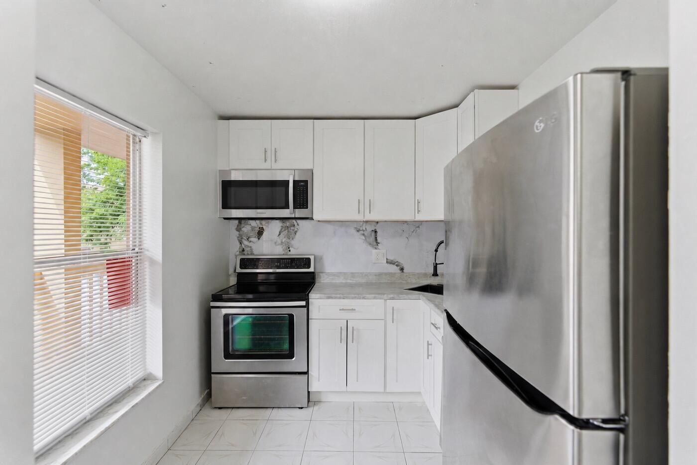 A small kitchen features white cabinets, stainless steel appliances, and a marble-patterned backsplash — 6020 NW 64th Avenue # 208, Tamarac FL 33319, TAMARAC, FL