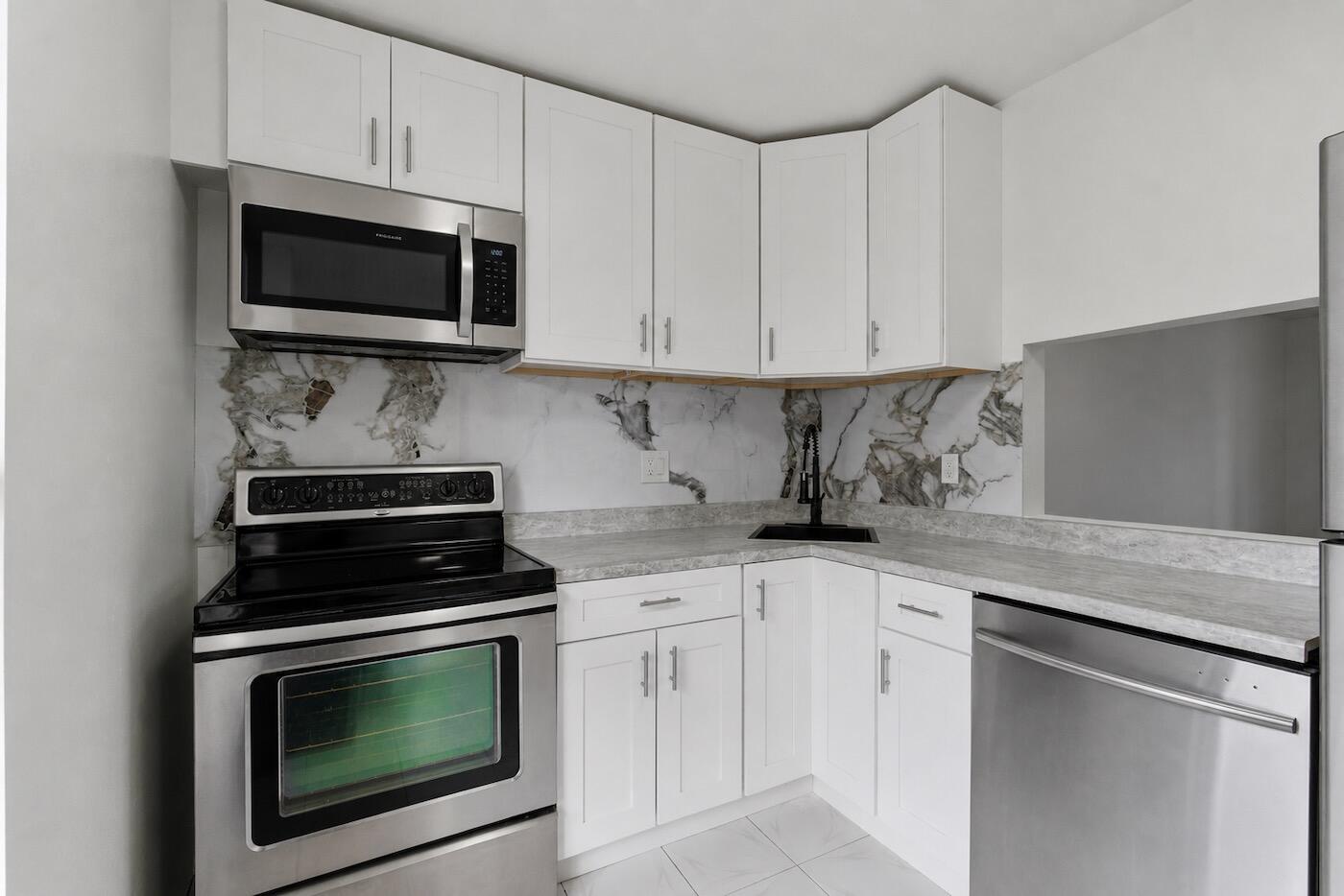 A kitchen with white cabinets, stainless steel appliances, and a marble-patterned backsplash — 6020 NW 64th Avenue # 208, Tamarac FL 33319, TAMARAC, FL