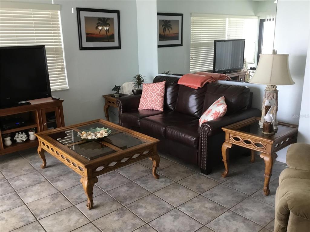 A living room features a brown leather sofa, wooden coffee table, and tiled flooring — 1571 S ATLANTIC AVENUE UNIT 406, NEW SMYRNA BEACH, FL