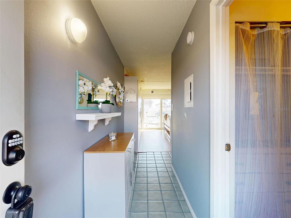 A hallway with light blue walls, tile flooring, a console table, and a mirror — 3700 S ATLANTIC AVENUE UNIT 103, NEW SMYRNA BEACH, FL