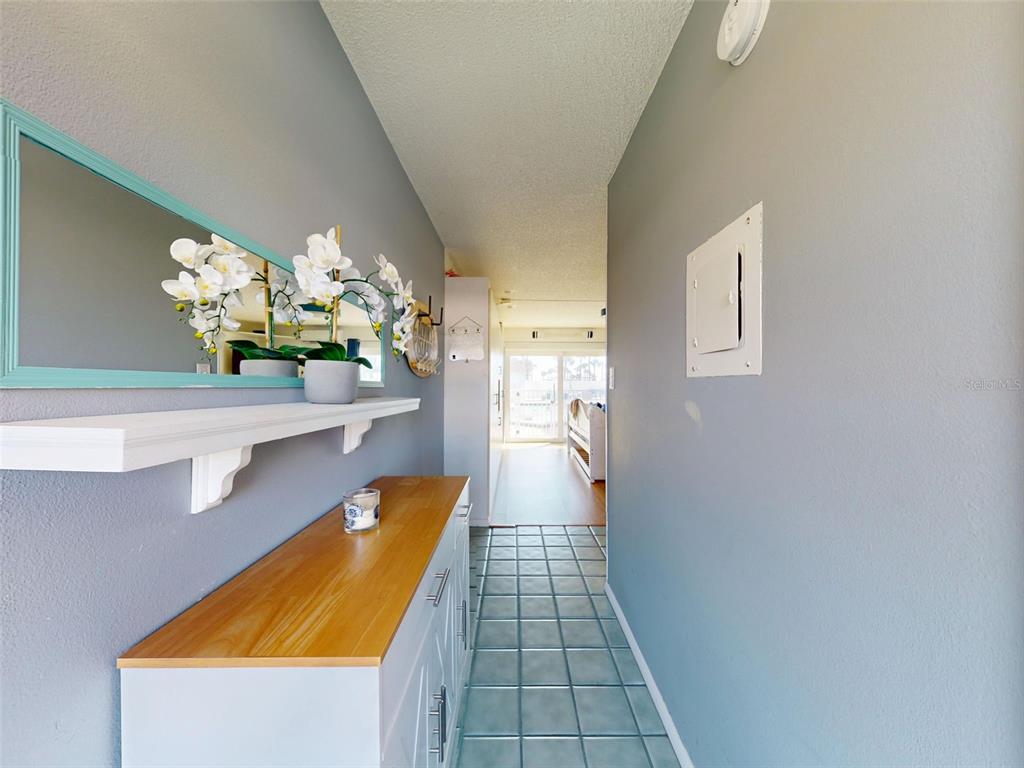 A hallway features a white console table, a wall-mounted shelf, and a mirror with a teal frame — 3700 S ATLANTIC AVENUE UNIT 103, NEW SMYRNA BEACH, FL