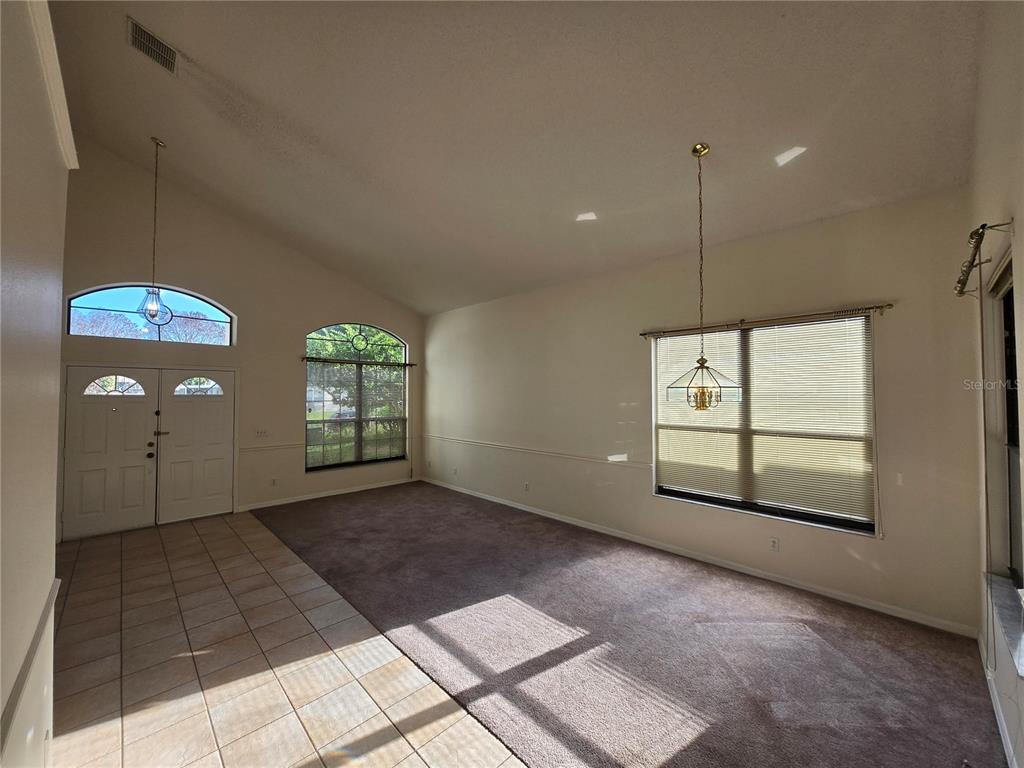 An open living area features vaulted ceilings, tiled entryway, carpeted flooring, and large windows — 12018 GRECO, ORLANDO, FL