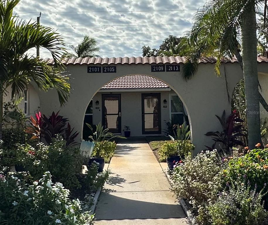 A walkway leads through a large arched entryway toward two residential unit doors — 2105 PUEBLO CIRCLE UNIT V2, SARASOTA, FL