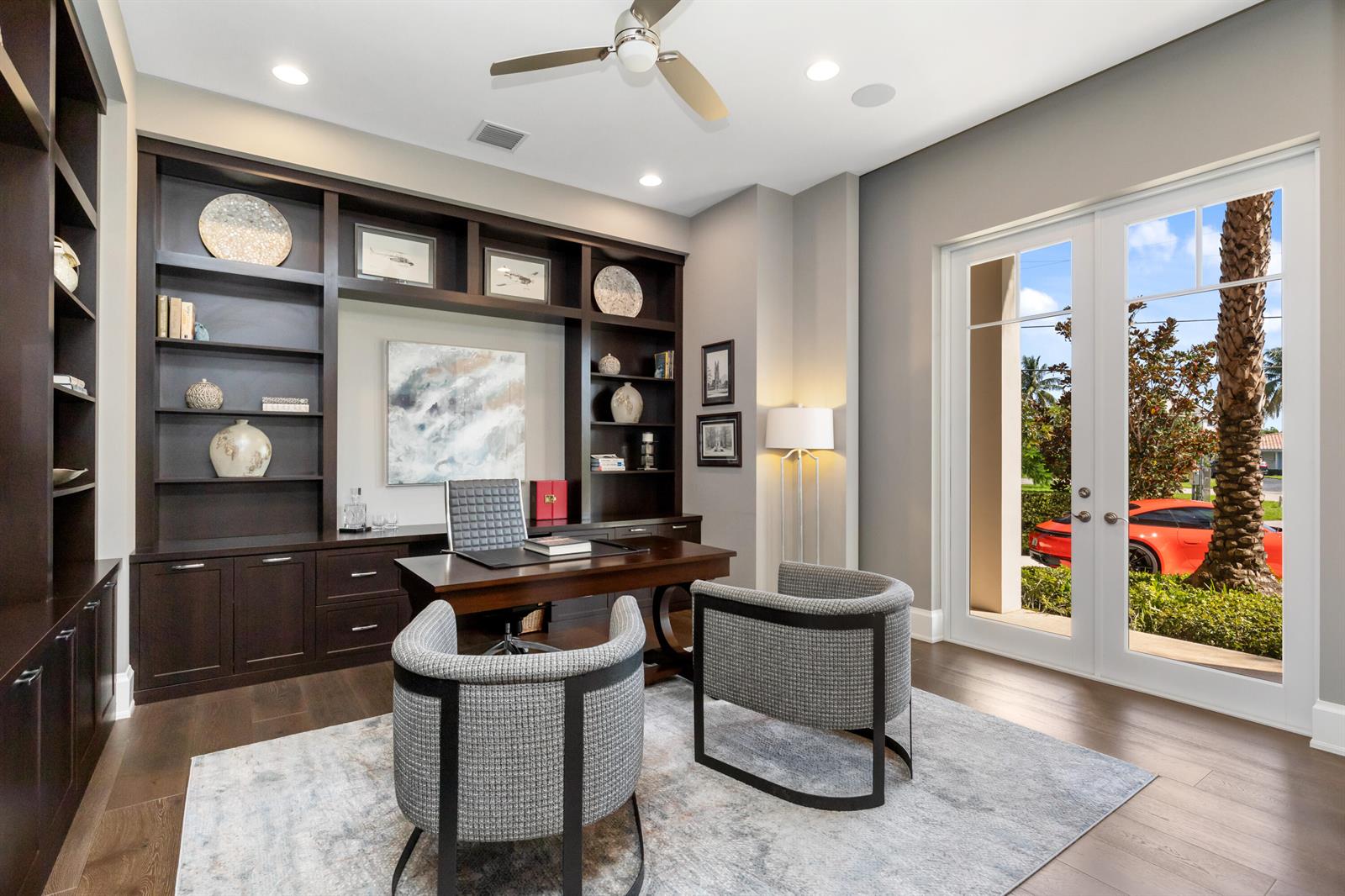 A home office features dark wood built-in shelving, a desk, two chairs, and glass doors — 3211 NE 27th Avenue, Lighthouse Point FL 33064, LIGHTHOUSE POINT, FL