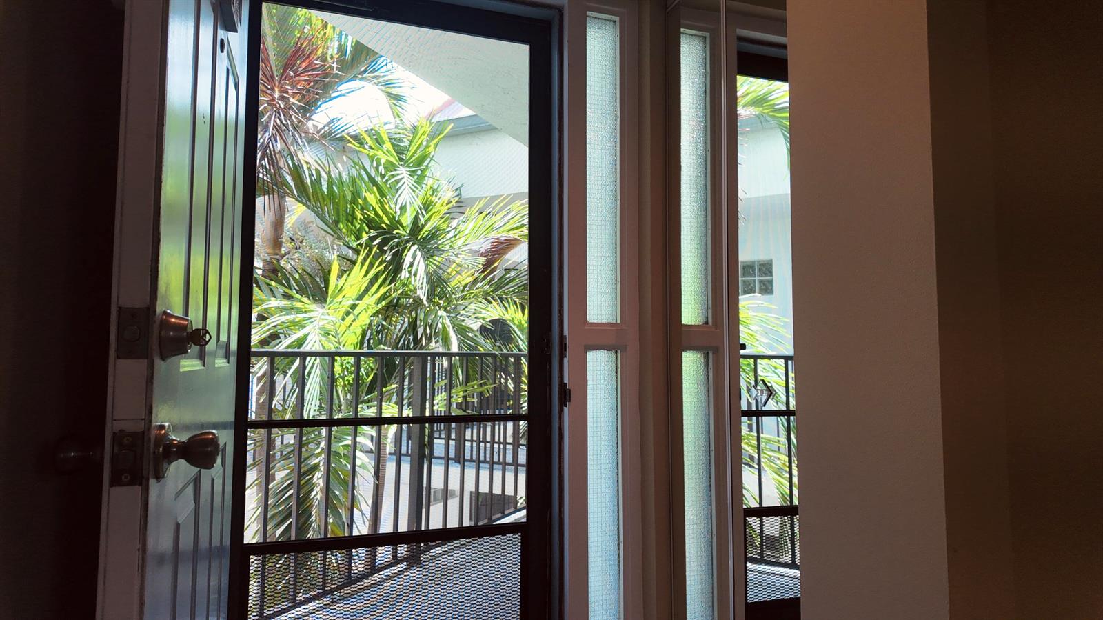 An open door and window look out onto a balcony with palm trees and foliage — 5418 Firenze Drive # P, Boynton Beach FL 33437, BOYNTON BEACH, FL