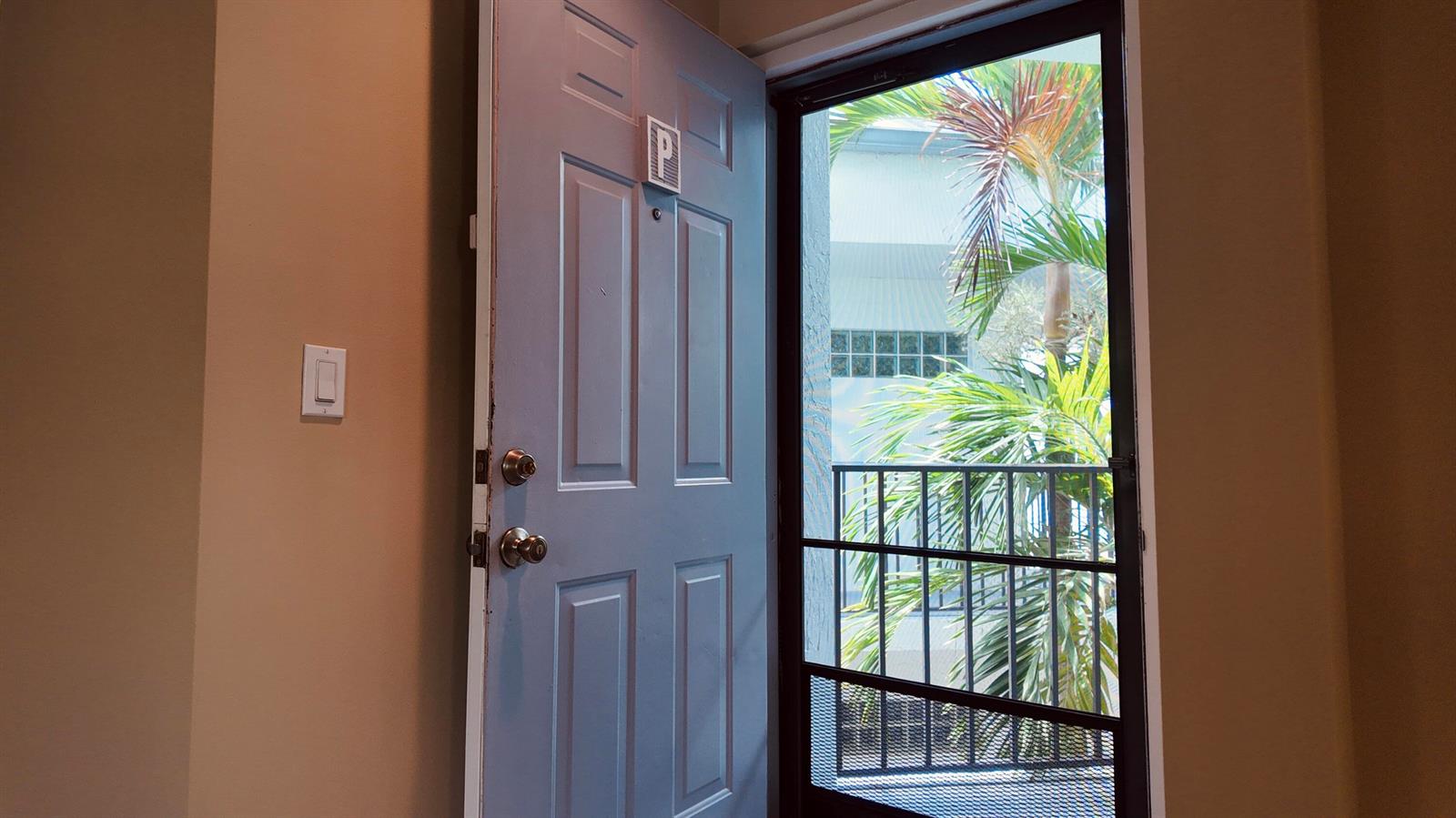 An open door reveals a view of a balcony with palm trees and a building — 5418 Firenze Drive # P, Boynton Beach FL 33437, BOYNTON BEACH, FL
