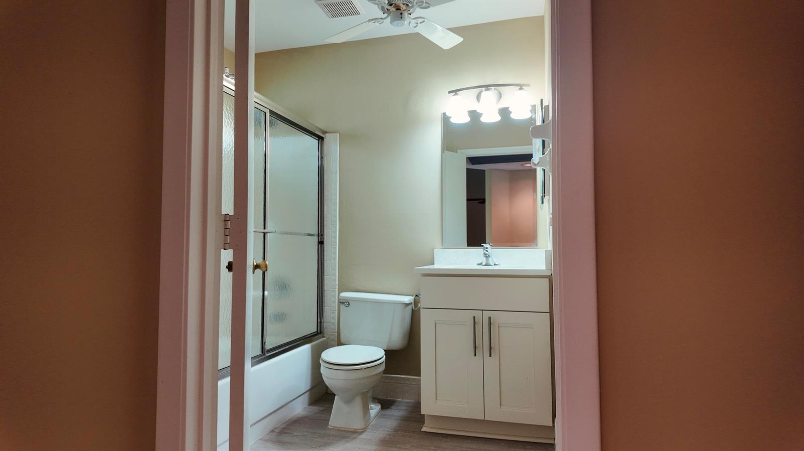 A bathroom featuring a vanity, a toilet, and a shower-tub combination with sliding glass doors — 5418 Firenze Drive # P, Boynton Beach FL 33437, BOYNTON BEACH, FL