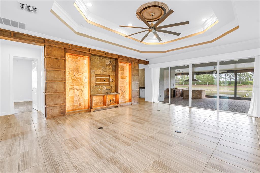 A living room with tile floors, a tray ceiling, and a stone-accented media wall — 15939 CAPE CORAL DRIVE, WIMAUMA, FL