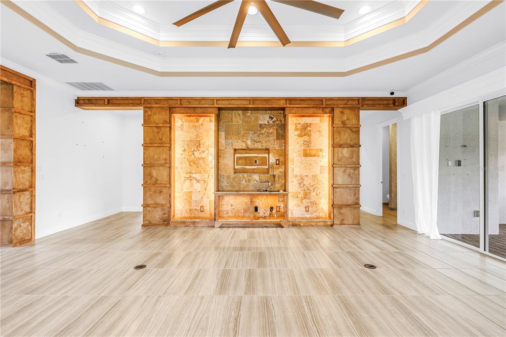 A living room features a stone-accented media wall, built-in wooden shelving, and light-colored tile flooring — 15939 CAPE CORAL DRIVE, WIMAUMA, FL