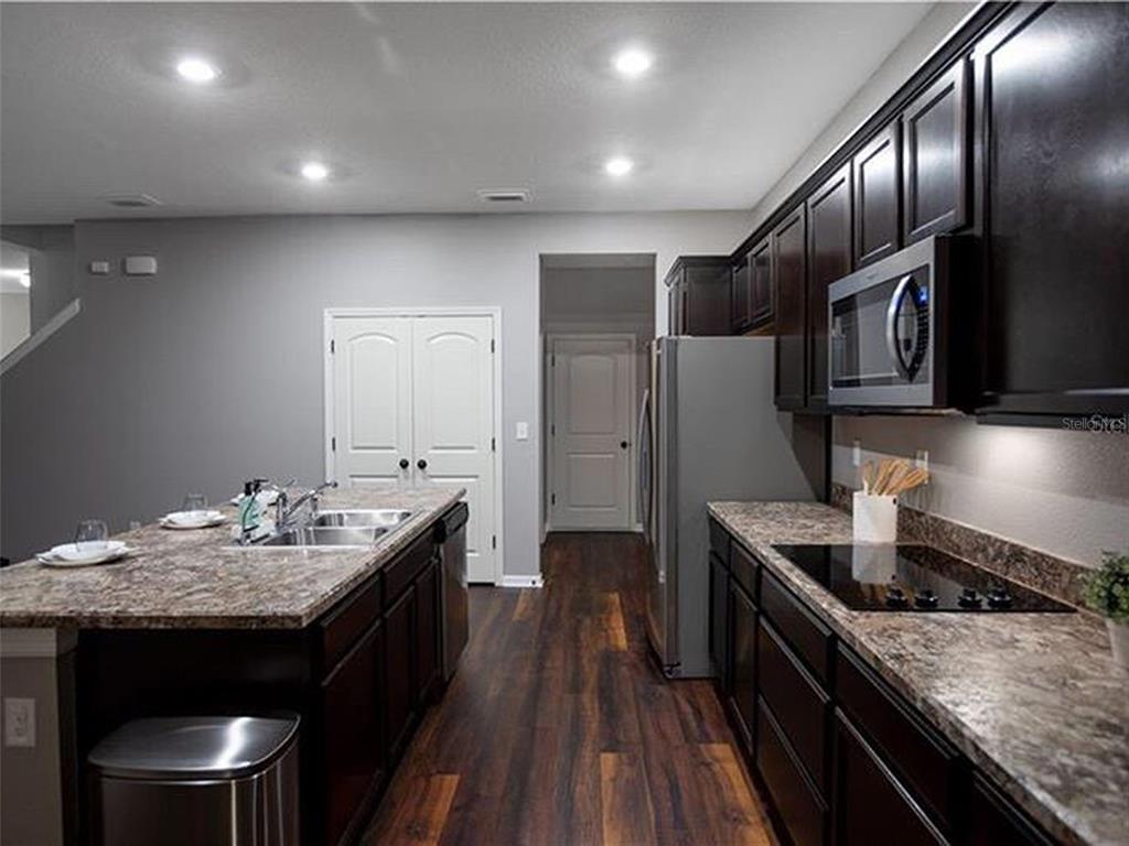 A kitchen with dark wood cabinets, granite countertops, stainless steel appliances, and wood-look flooring — 9318 EQUITY LANE, SEFFNER, FL