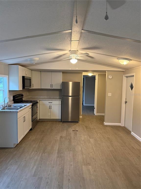 A kitchen with white cabinets, stainless steel appliances, and light wood-look flooring — 9195 SE 142ND PLACE, SUMMERFIELD, FL