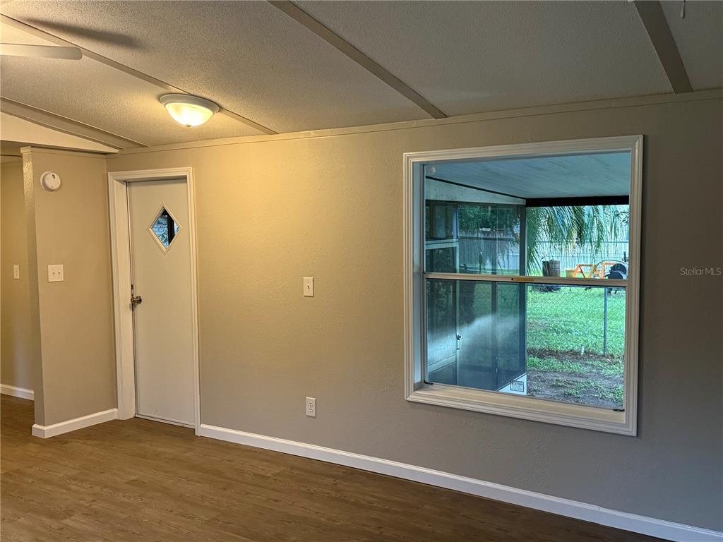 A room with light gray walls, wood-look flooring, a white door, and a large window — 9195 SE 142ND PLACE, SUMMERFIELD, FL