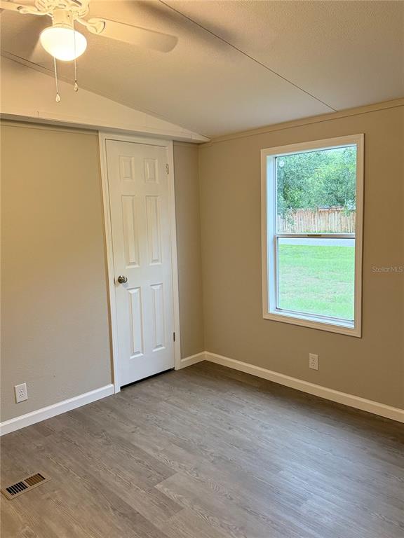 An empty bedroom features light-colored walls, wood-look flooring, a ceiling fan, and a single window — 9195 SE 142ND PLACE, SUMMERFIELD, FL