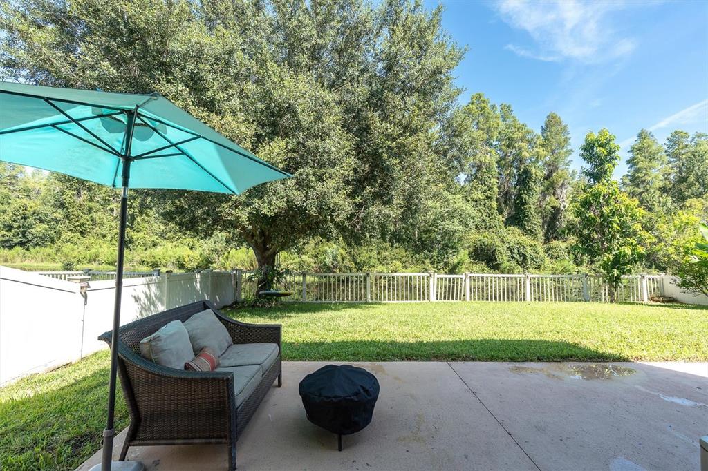 A backyard patio features a wicker sofa, a turquoise umbrella, and a view of trees — 1307 KETZAL DRIVE, TRINITY, FL