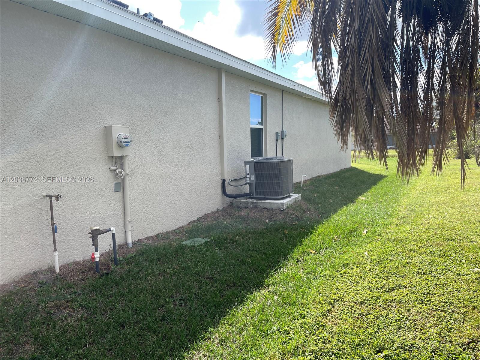 The exterior of a stucco house features an HVAC unit, utility meters, and plumbing pipes — 455 Londrina Dr, Punta Gorda FL 33983, PUNTA GORDA, FL