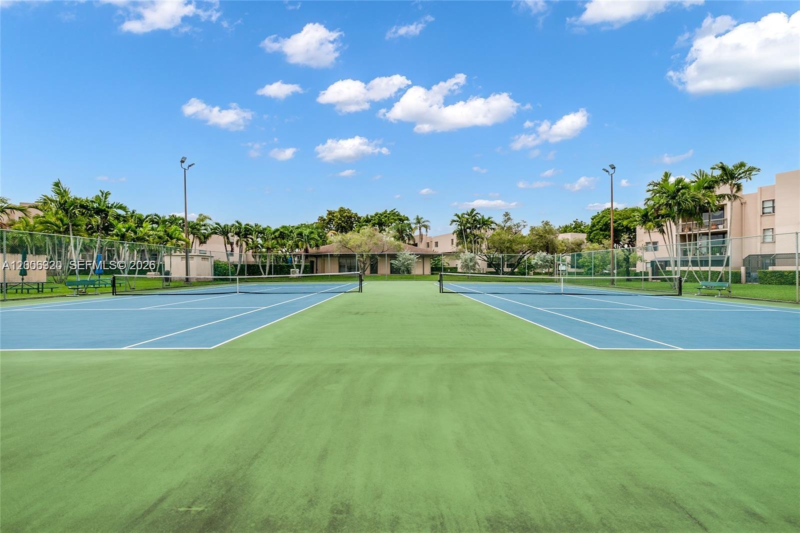 Two outdoor tennis courts with blue surfaces and green borders are surrounded by palm trees — 10625 SW 112th Ave # 301, Miami FL 33176, MIAMI, FL