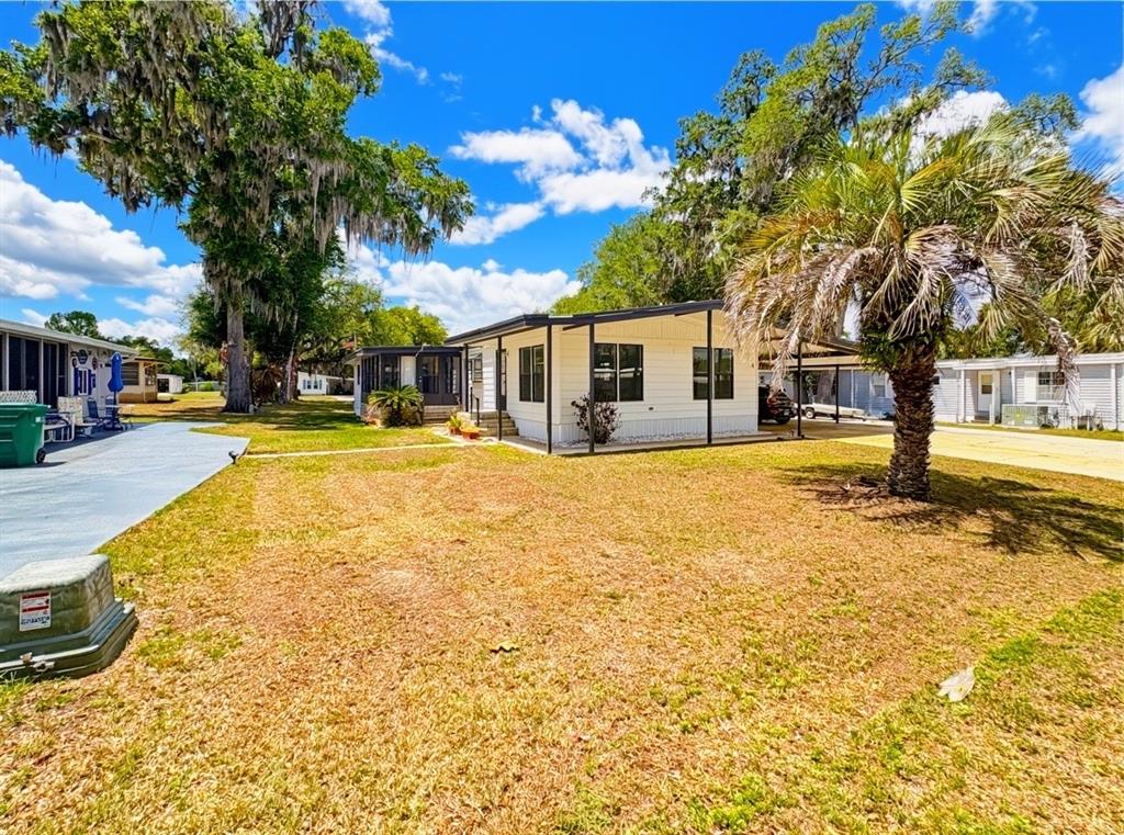 A white manufactured home with a covered porch sits on a grassy lot with trees — 4 E QUAIL RUN, WILDWOOD, FL